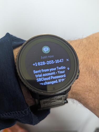 A smartwatch displays a notification about a password change from a Twilio trial account. (Captioned by AI)